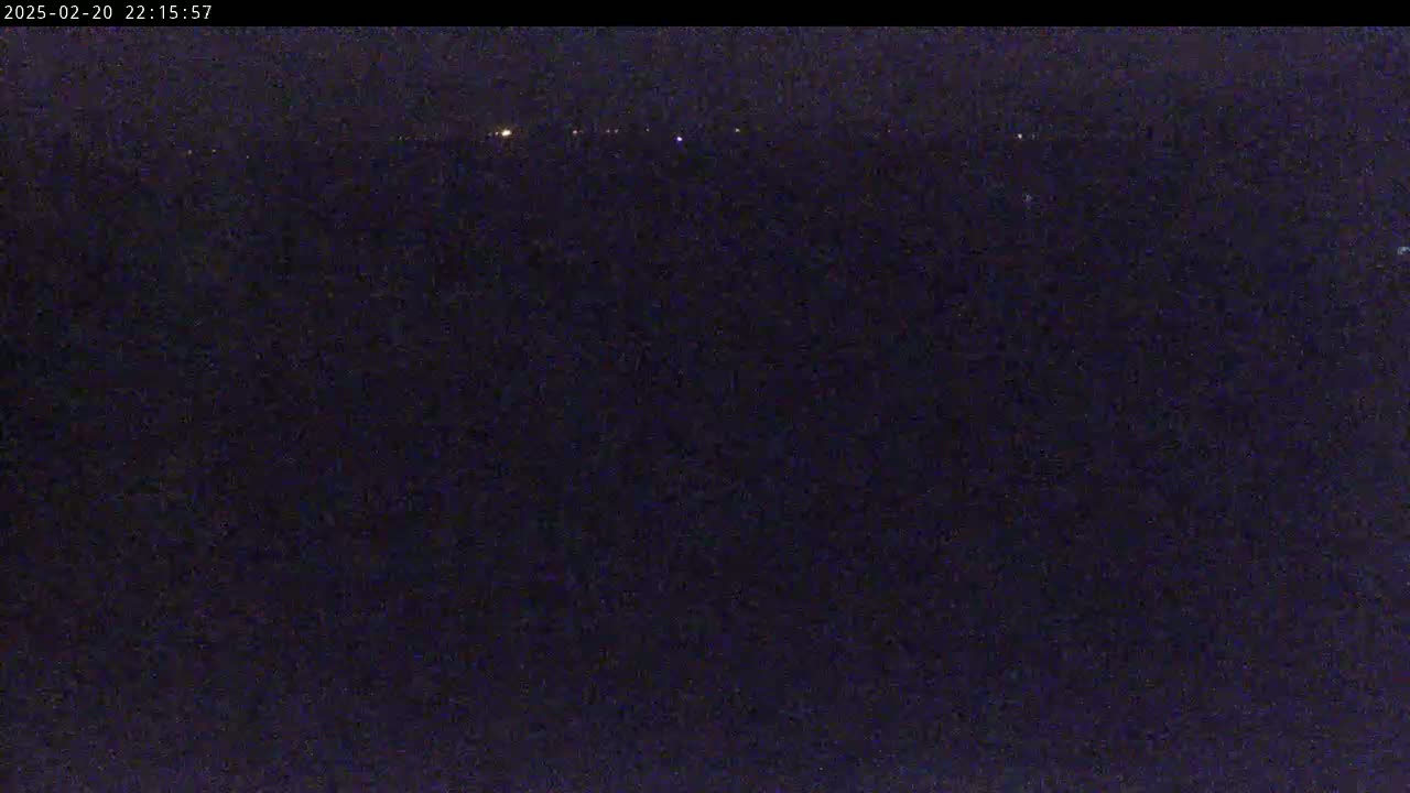 A dark, nighttime scene shows a distant line of faint lights against a very dark background.