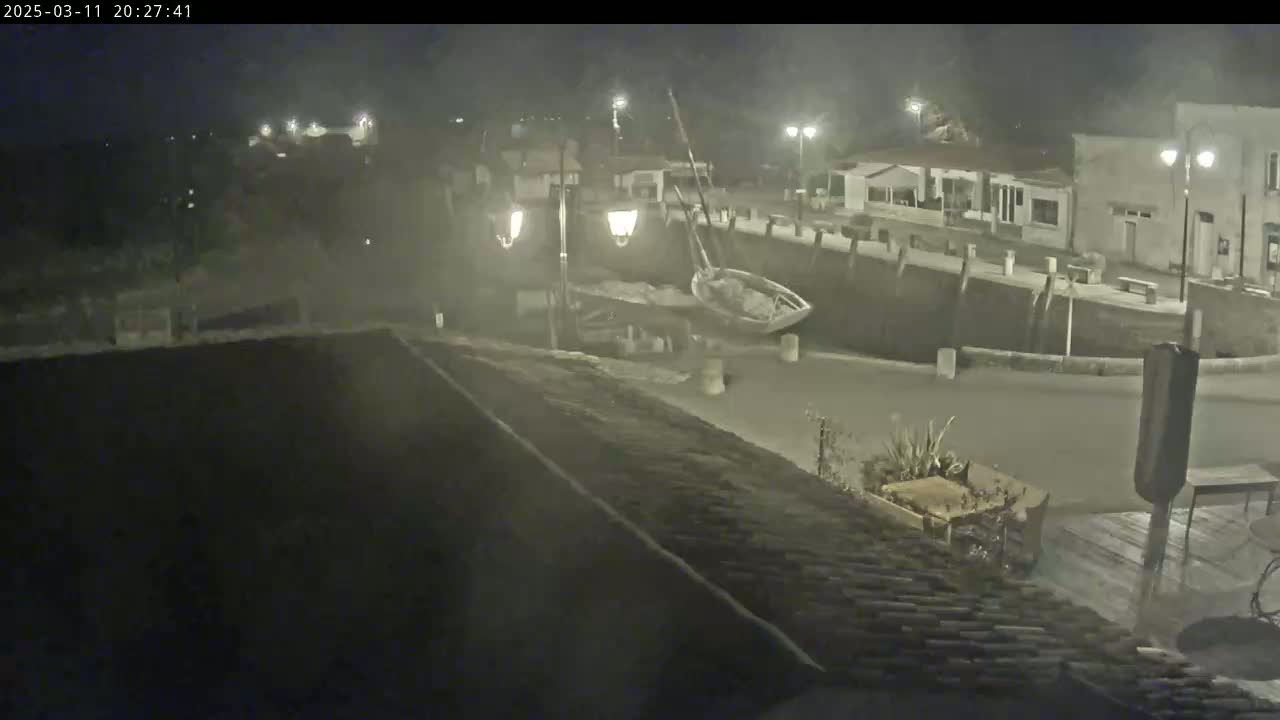 A nighttime view of a harbor scene with a small boat near a dock, under hazy or foggy conditions.
