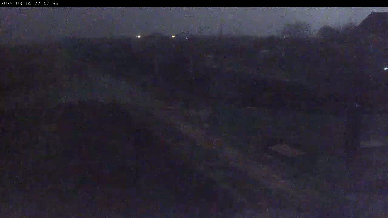 A dark, nighttime outdoor scene shows a dimly lit landscape with some distant lights under an overcast sky.