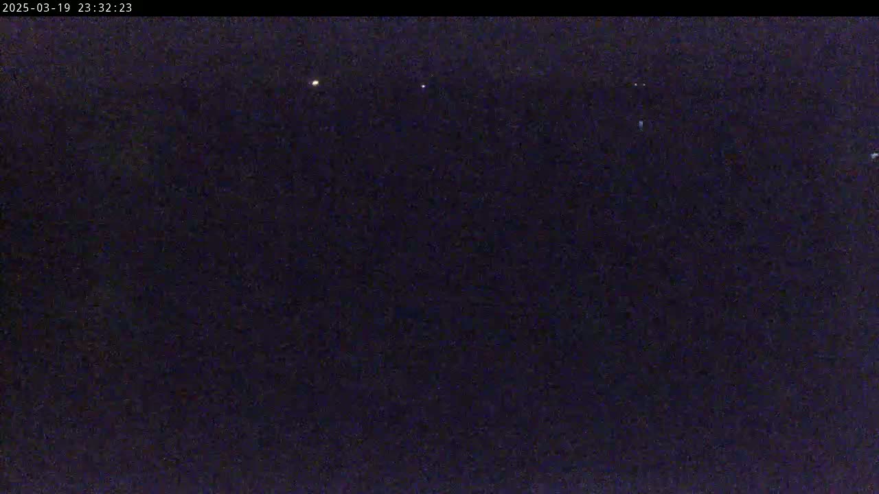 A dark nighttime scene shows a few faint lights in the distance under a clear, dark sky.