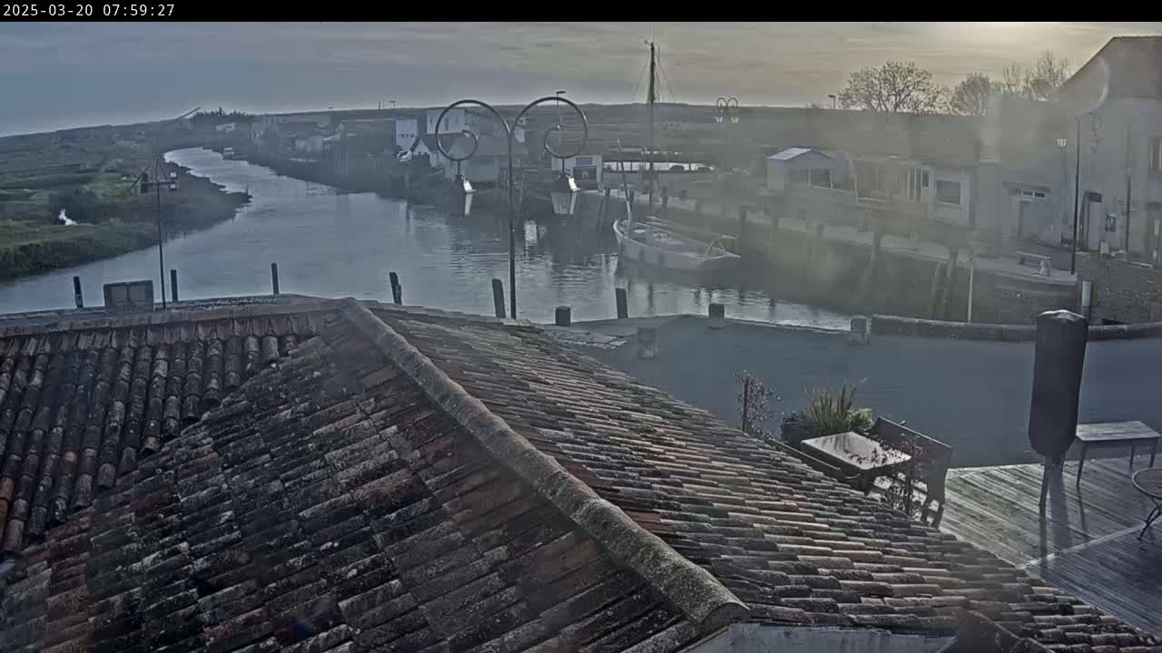 A hazy sunrise illuminates a waterway lined with buildings and boats, viewed from a tiled rooftop.