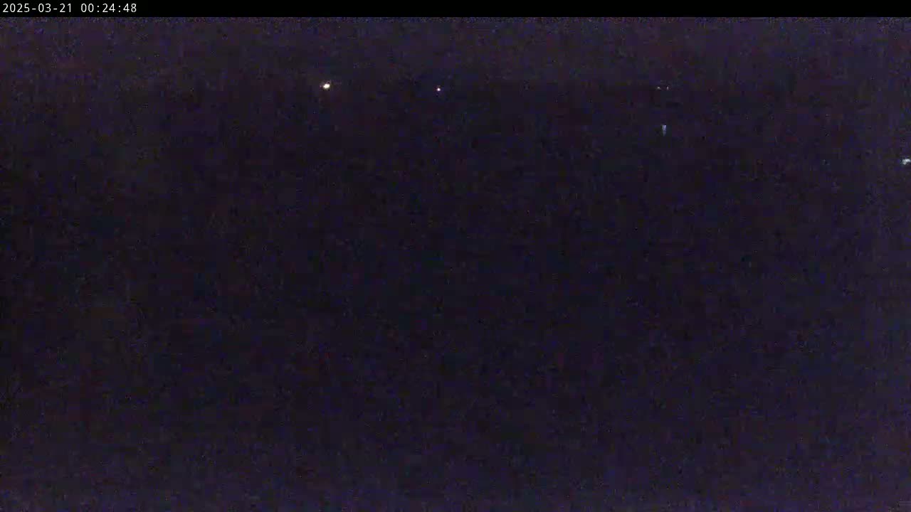A dark, nighttime scene shows several faint lights in the distance under a clear sky.