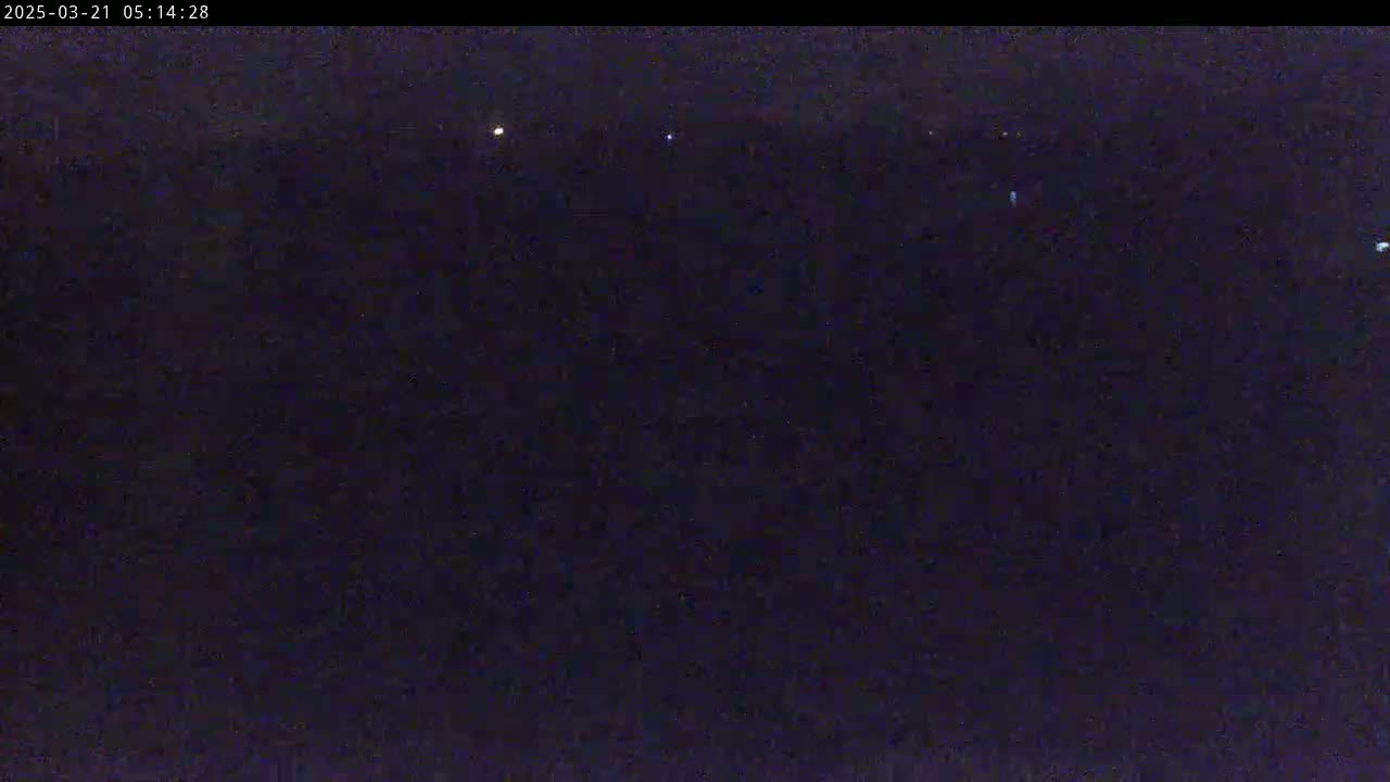 A nighttime, dark landscape is visible, with a few faint lights in the distance.