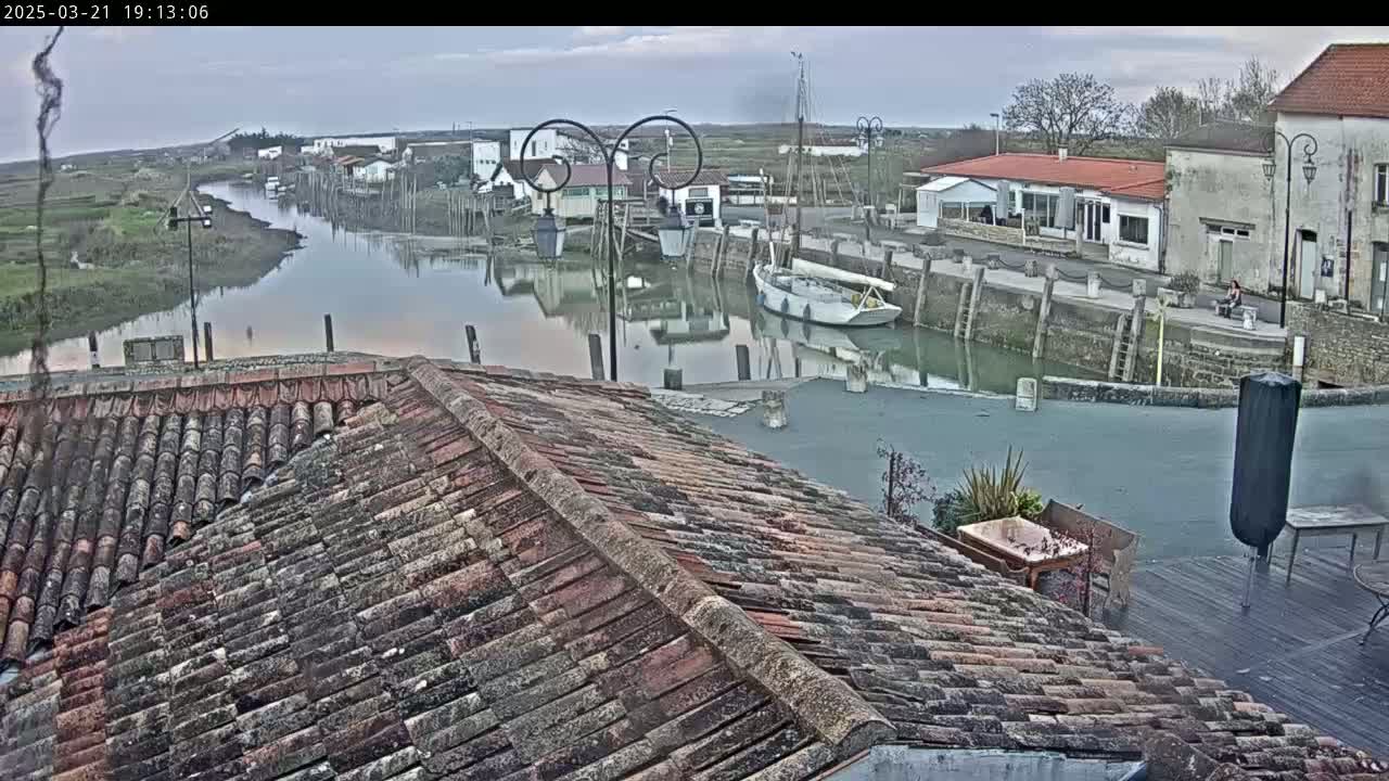 A tiled roof overlooks a calm waterway with docked boats and buildings under an overcast sky.