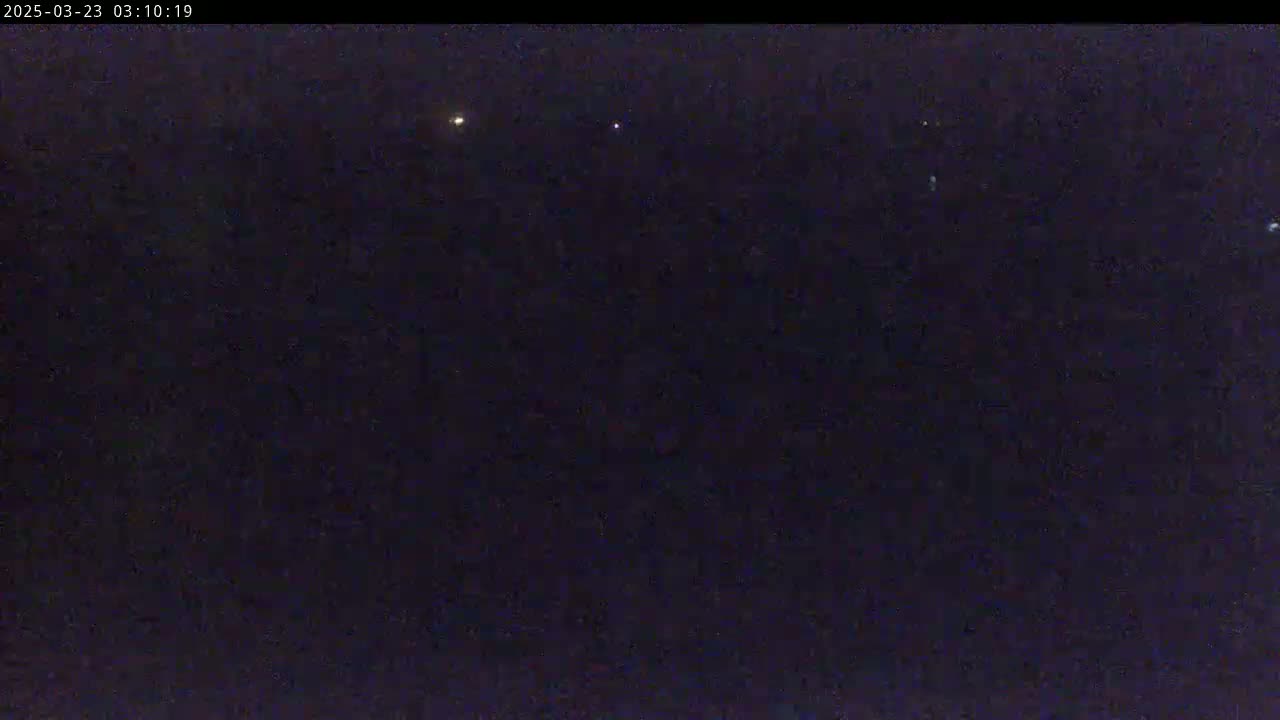 A dark, nighttime scene shows a few faint lights in the distance under a clear, dark sky.