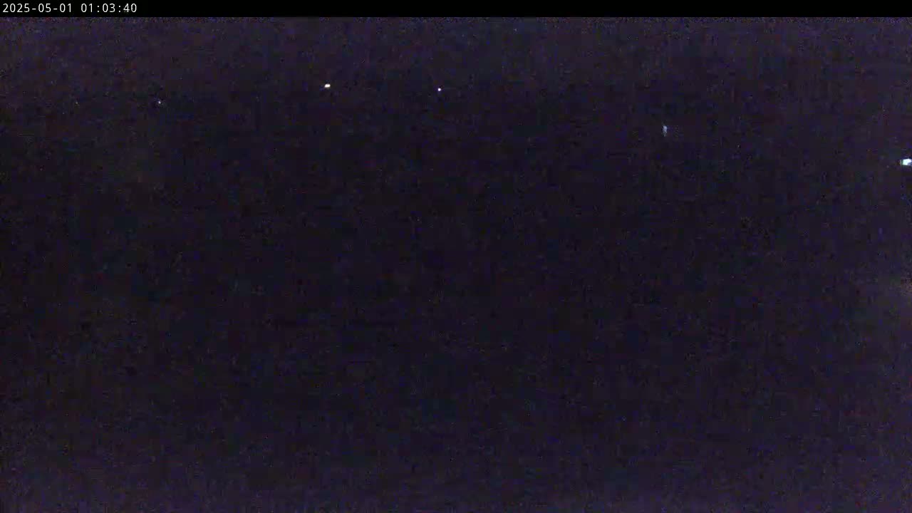 A dark, nighttime scene shows a few small, distant lights against a black background.