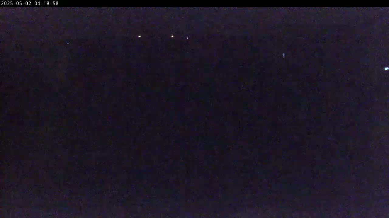 A dark nighttime scene shows a few faint lights in the distance under a clear, dark sky.