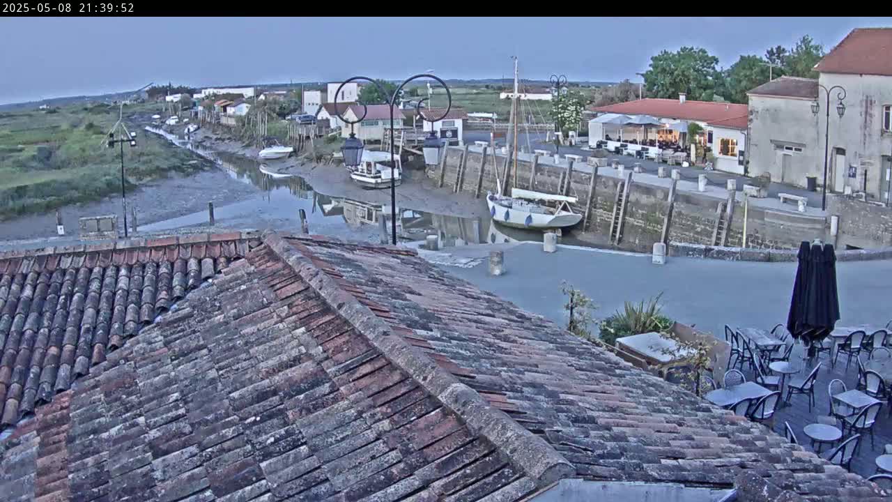 A low-light view from a tiled roof shows a harbor at low tide with several boats, buildings, and outdoor seating.