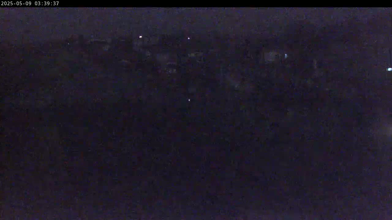 A dark, nighttime scene shows a blurry, indistinct mass of objects or structures illuminated by a few faint lights.