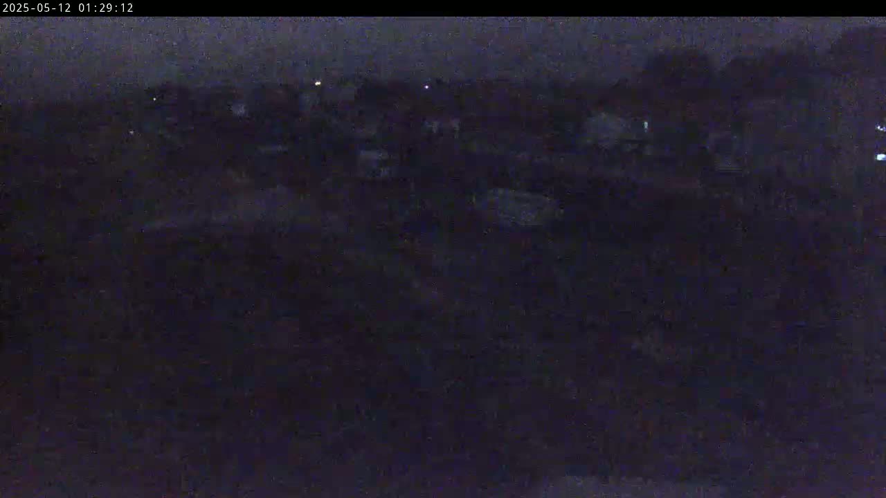 A dark, nighttime scene shows a collection of indistinct structures under a cloudy sky.