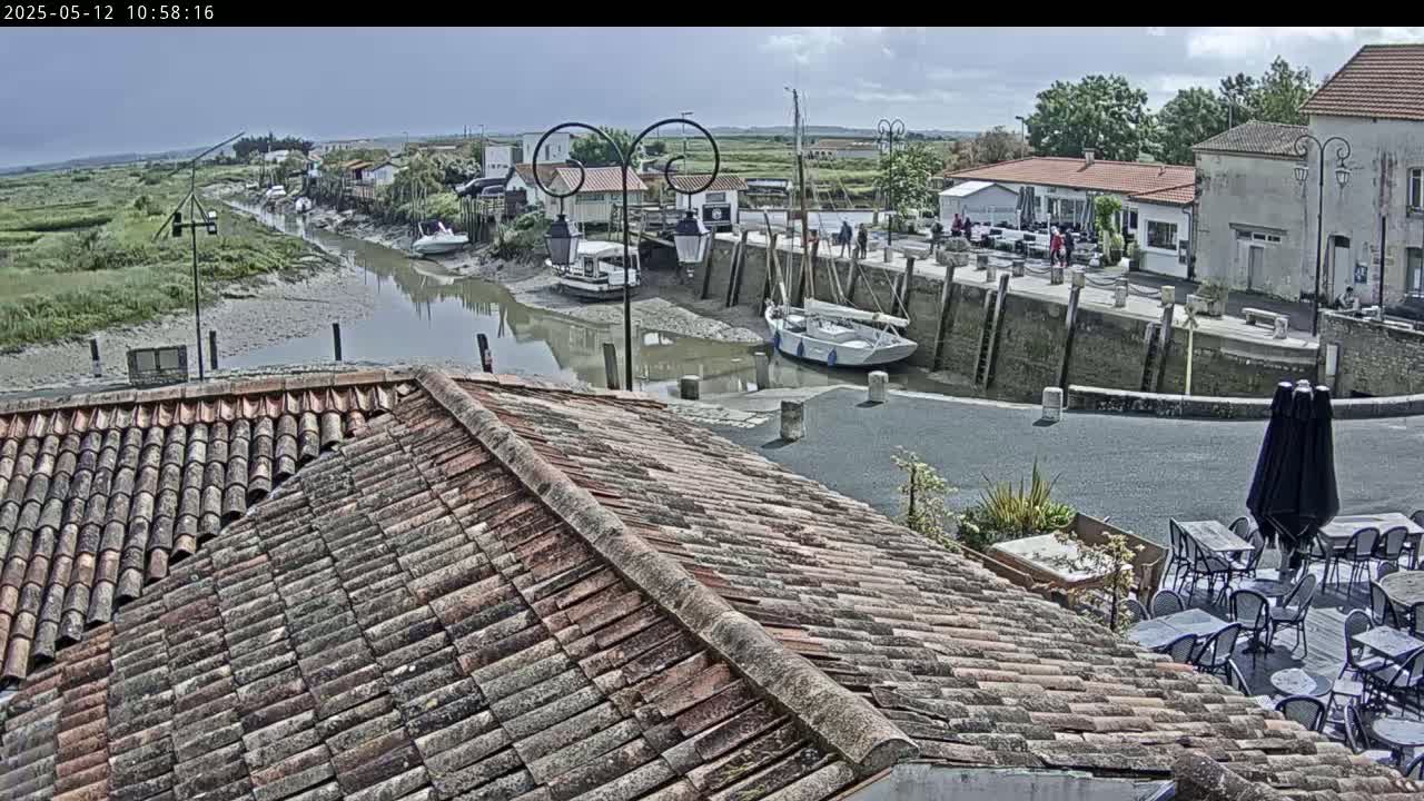 A mostly sunny view from a tiled roof shows a calm waterway with several boats docked near buildings and outdoor seating.