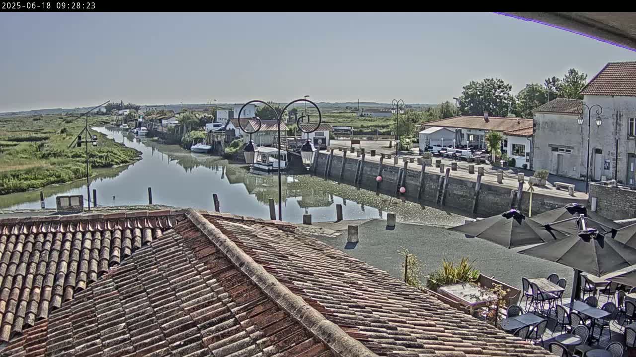 A sunny view overlooking a canal lined with buildings, boats, and outdoor seating areas.