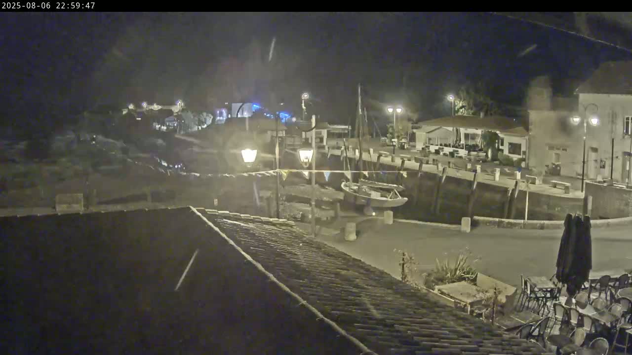 A nighttime view of a small harbor with boats and buildings under light rain.