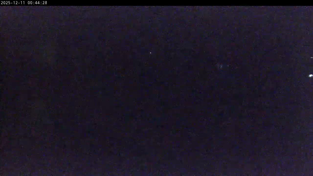 The image displays a very dark, grainy night sky with several faint white lights, suggesting clear weather.