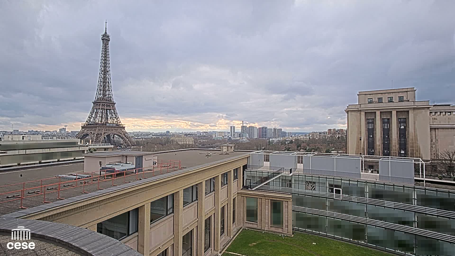 A rooftop view of Paris on an overcast day, showing the Eiffel Tower in the distance and modern buildings in the foreground.