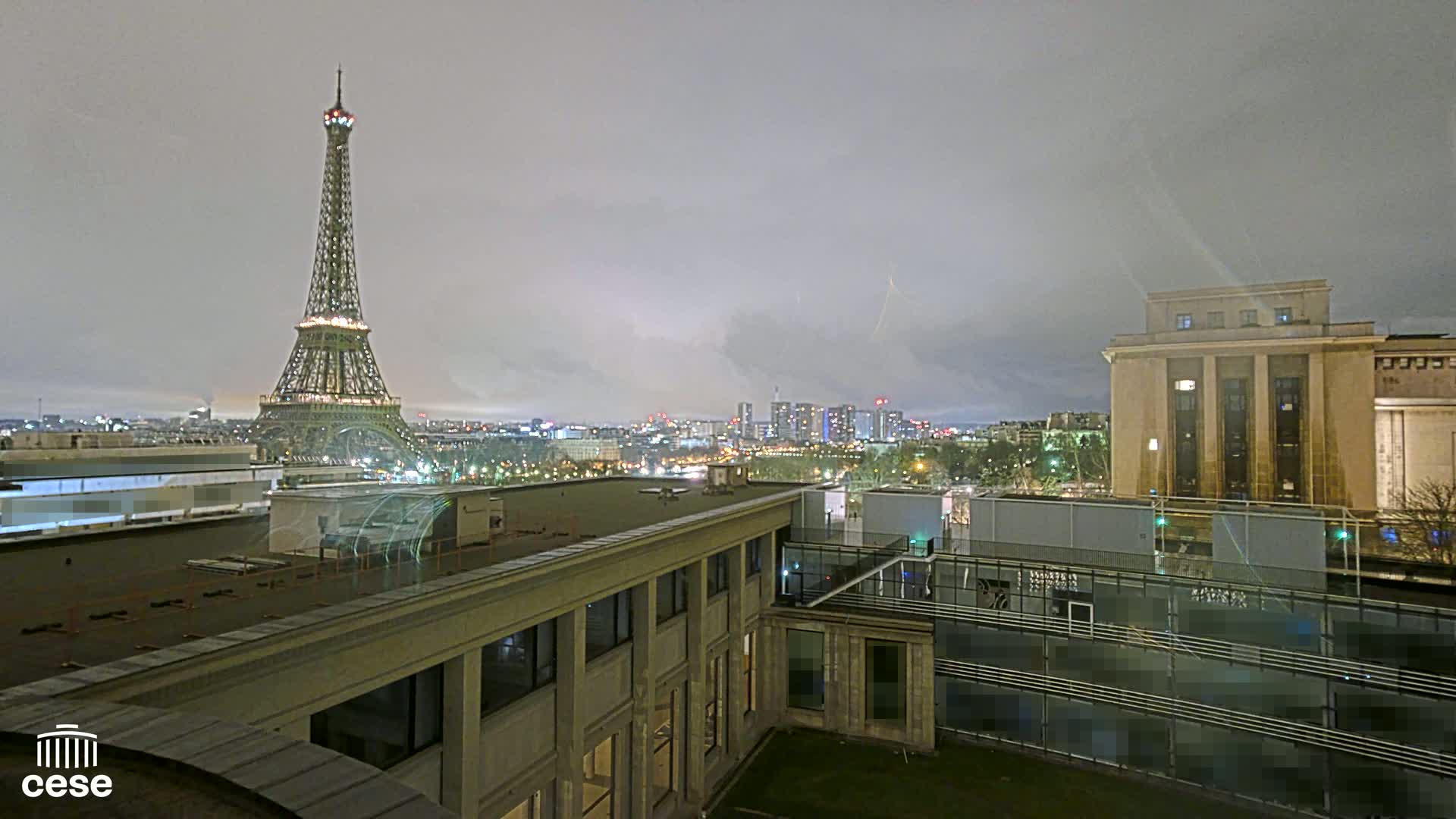 A nighttime view of the Eiffel Tower and a cityscape under an overcast sky.