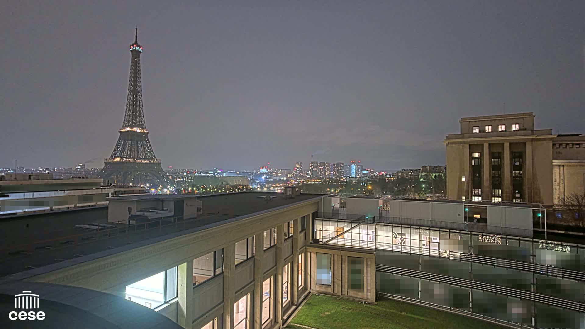 A nighttime view of the Eiffel Tower from a rooftop, showing a city skyline under a cloudy sky.