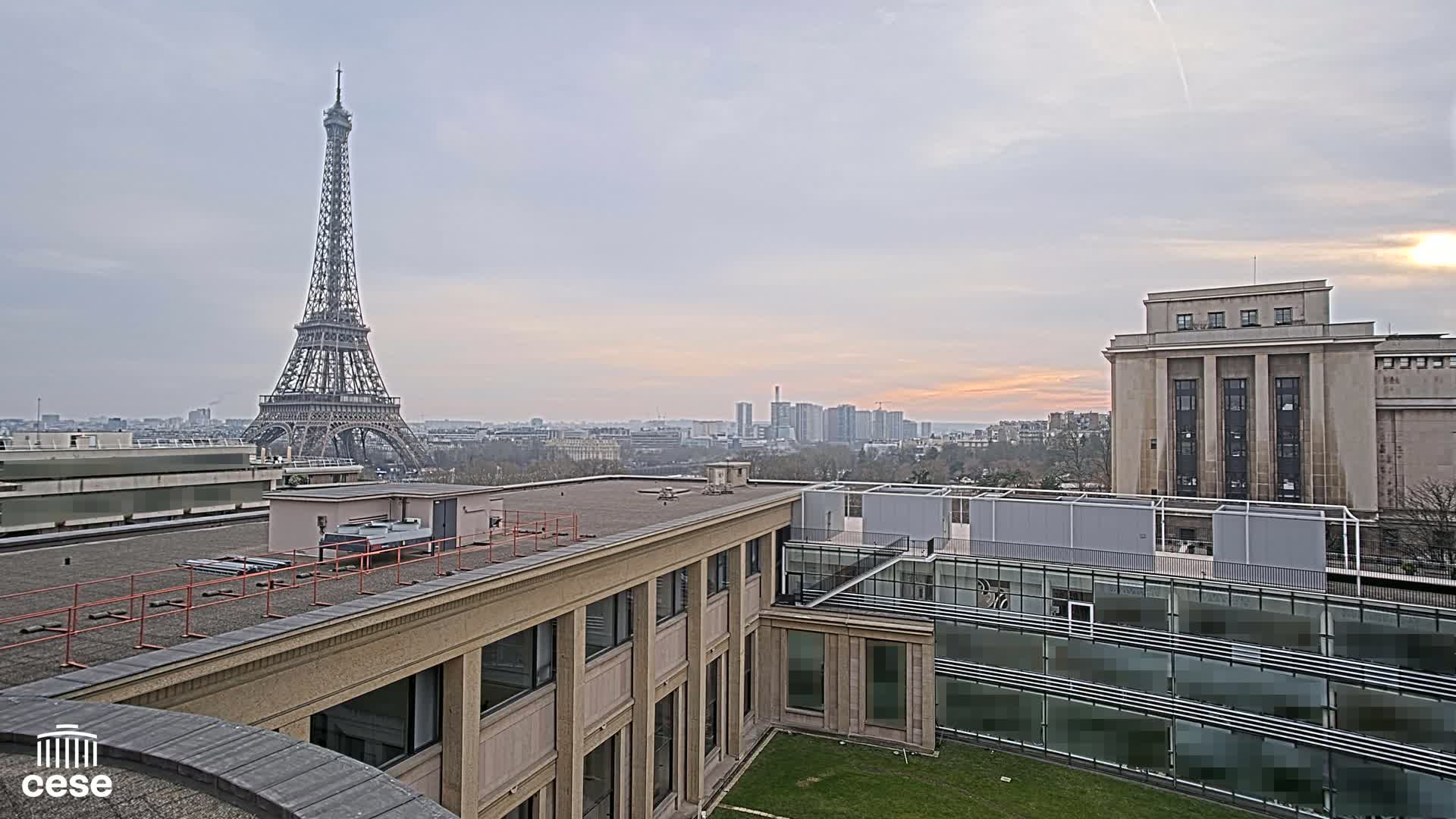 An overcast Parisian cityscape is seen from a rooftop, featuring the Eiffel Tower in the distance and modern buildings in the foreground.