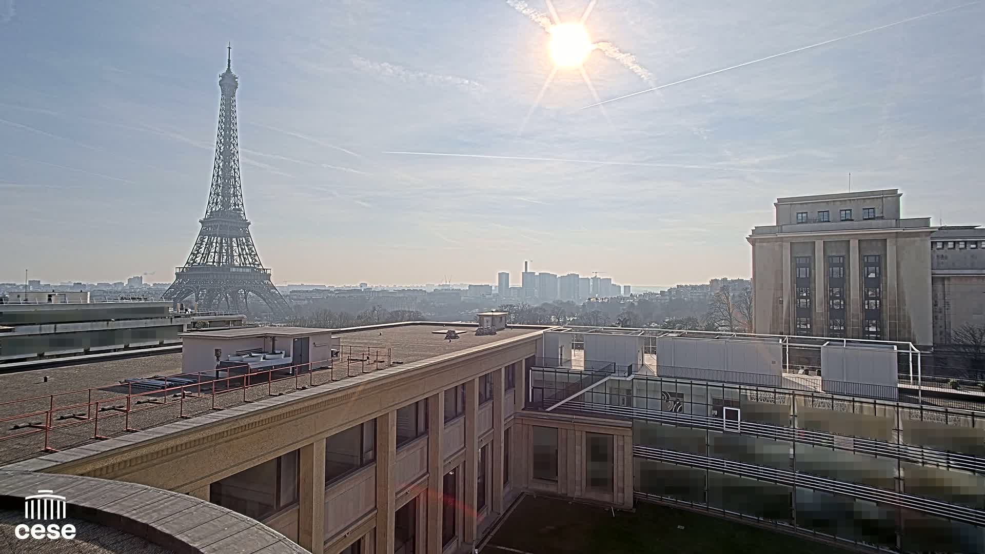 A sunny day in Paris shows the Eiffel Tower in the distance, viewed from a rooftop overlooking other buildings.