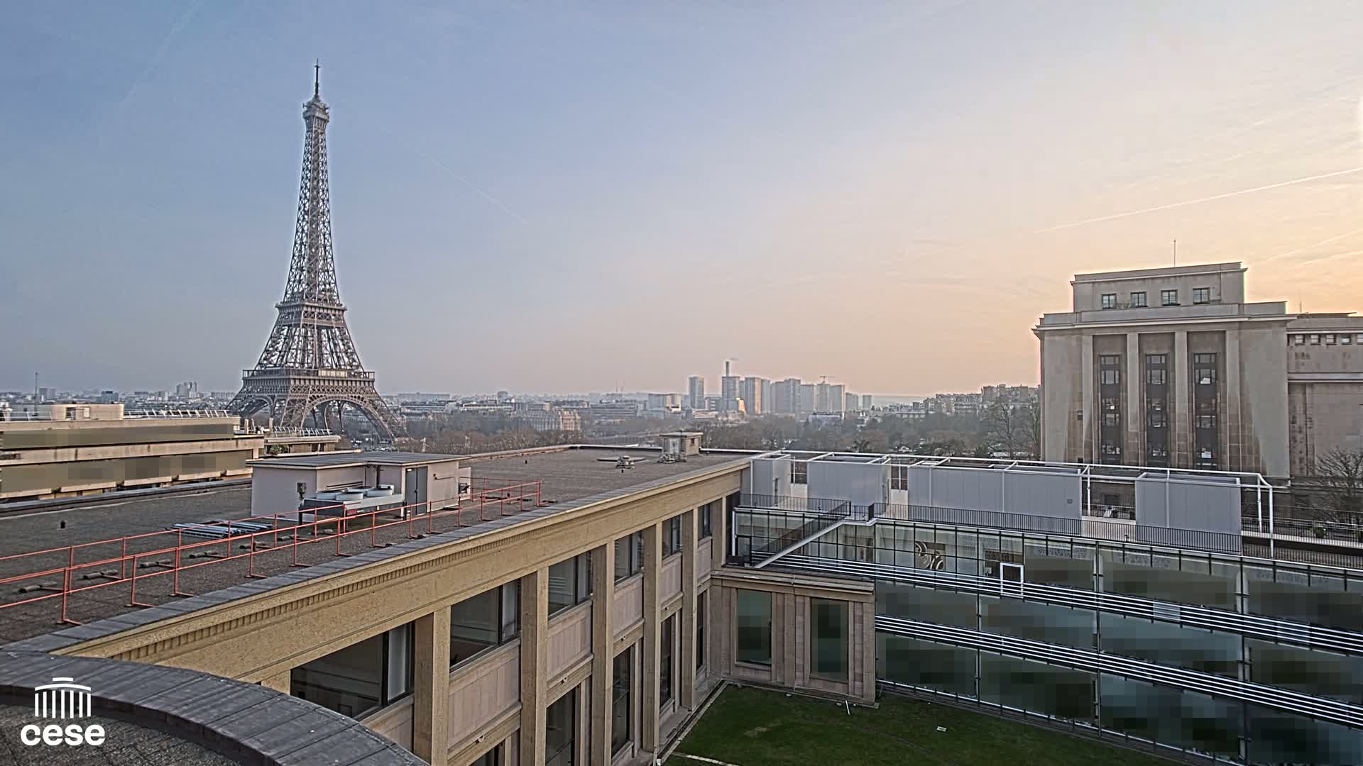 A rooftop view of the Eiffel Tower in the distance on a clear, light-pink sunset.