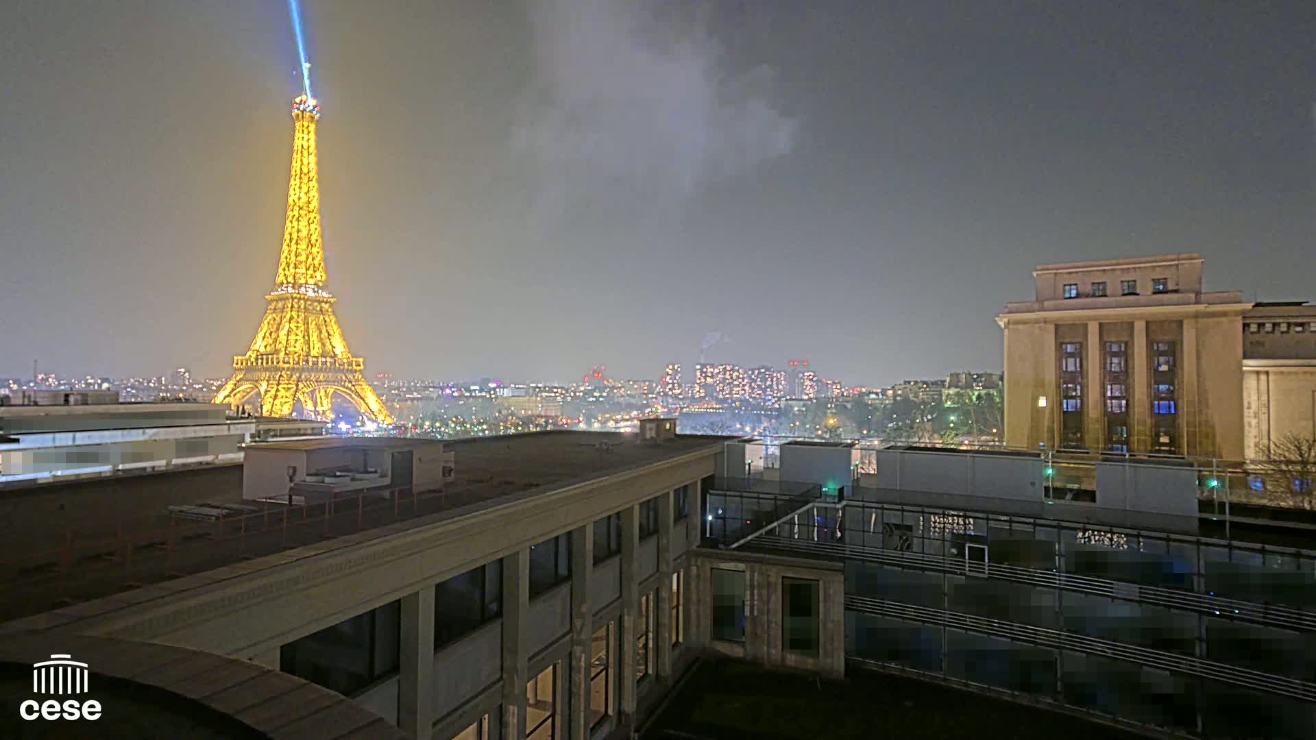 A nighttime view of the Eiffel Tower illuminated,  a cityscape, and a building, under a cloudy sky.