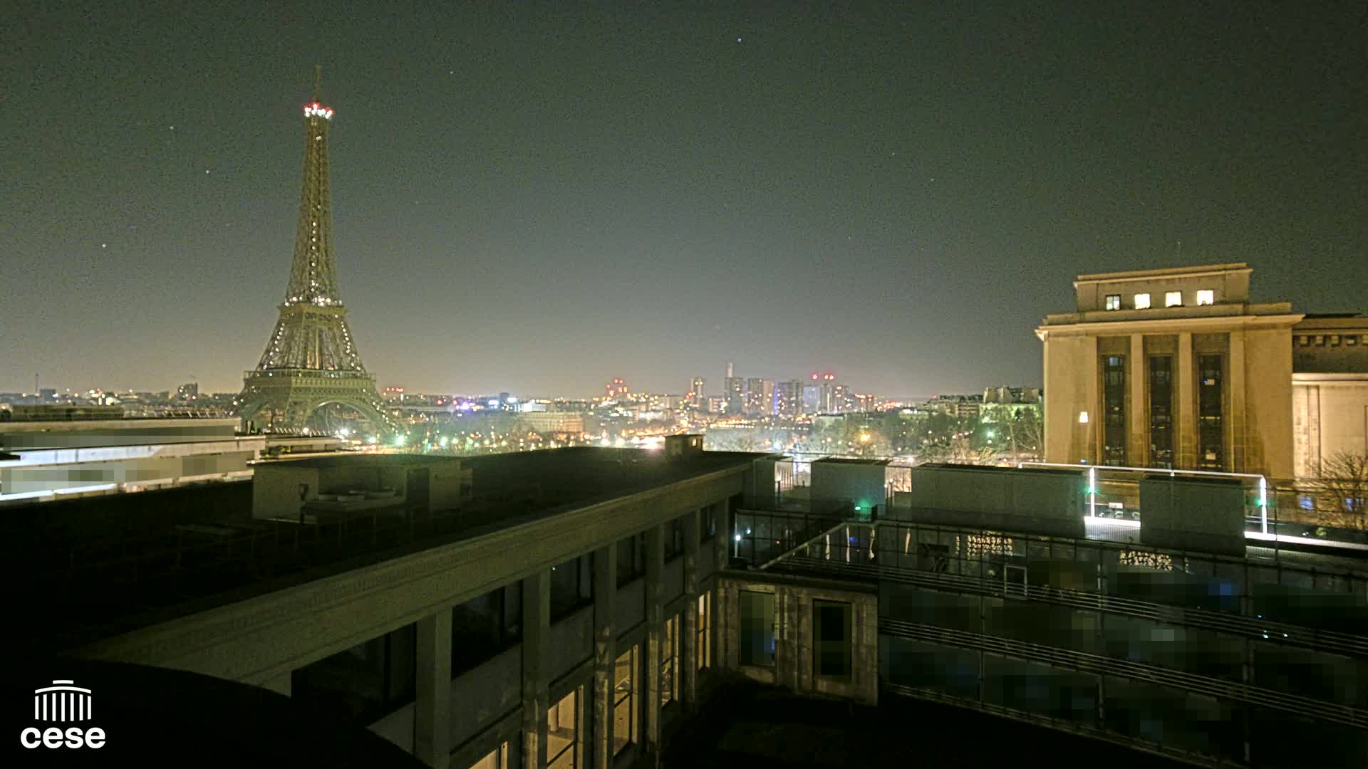 A nighttime view of the Eiffel Tower and a cityscape, seen from a rooftop building.