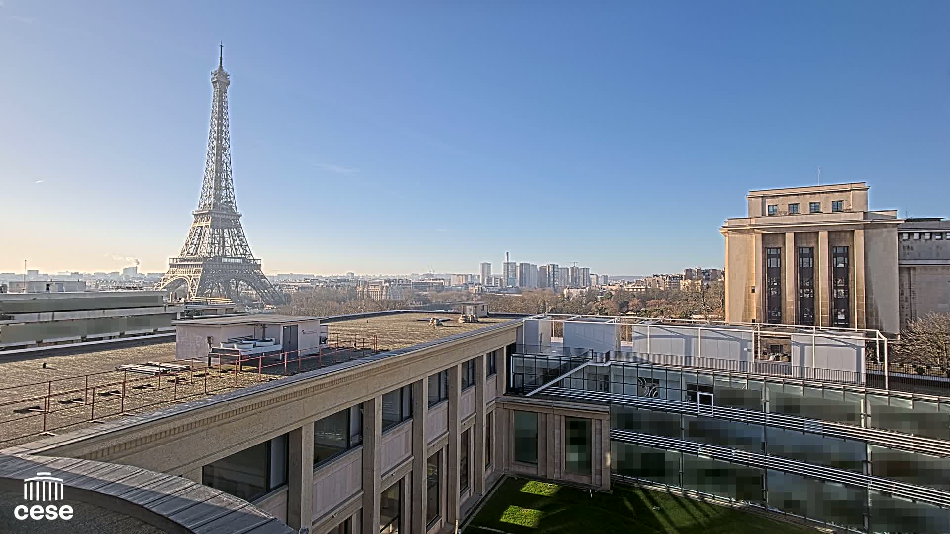 A rooftop view of Paris on a sunny day, showcasing the Eiffel Tower in the distance and city buildings in the foreground.