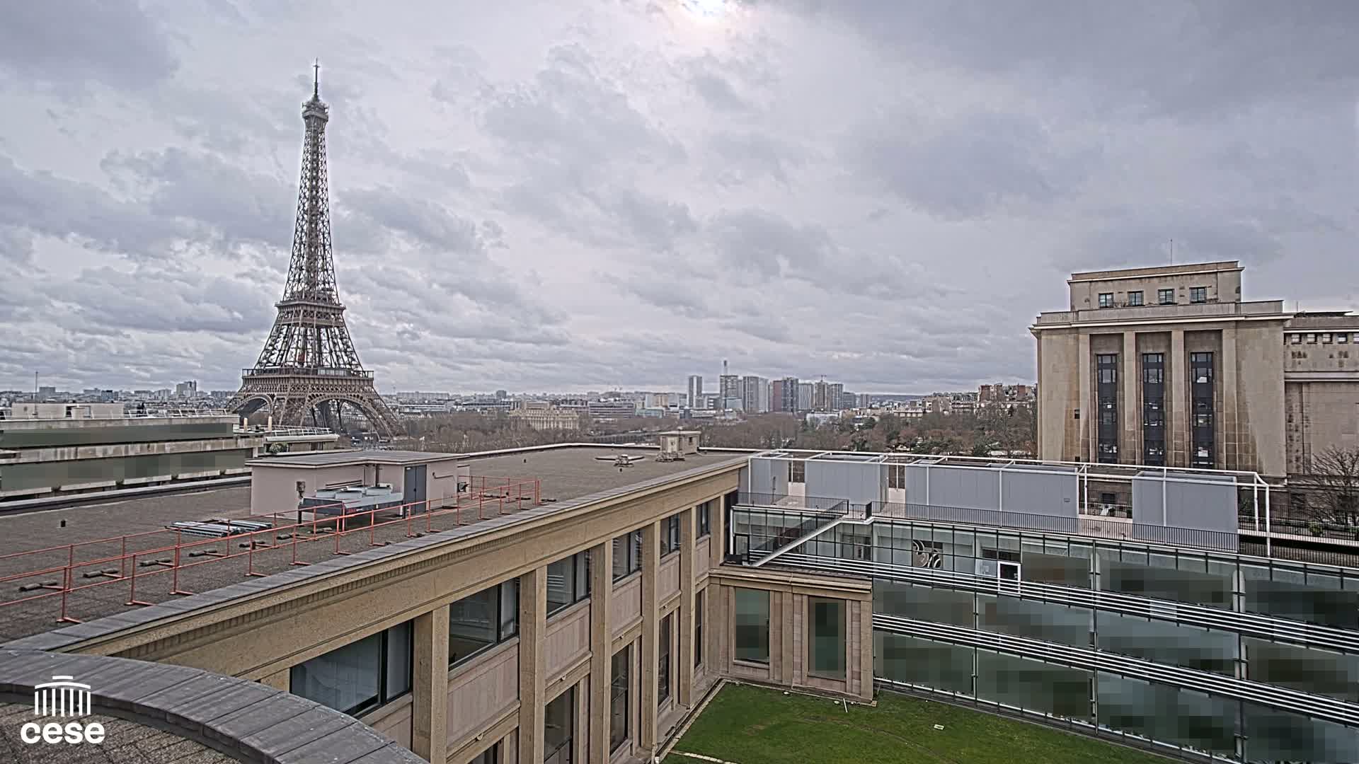 A high-angle view of a cityscape on an overcast day, featuring the Eiffel Tower in the distance and a large building in the foreground.