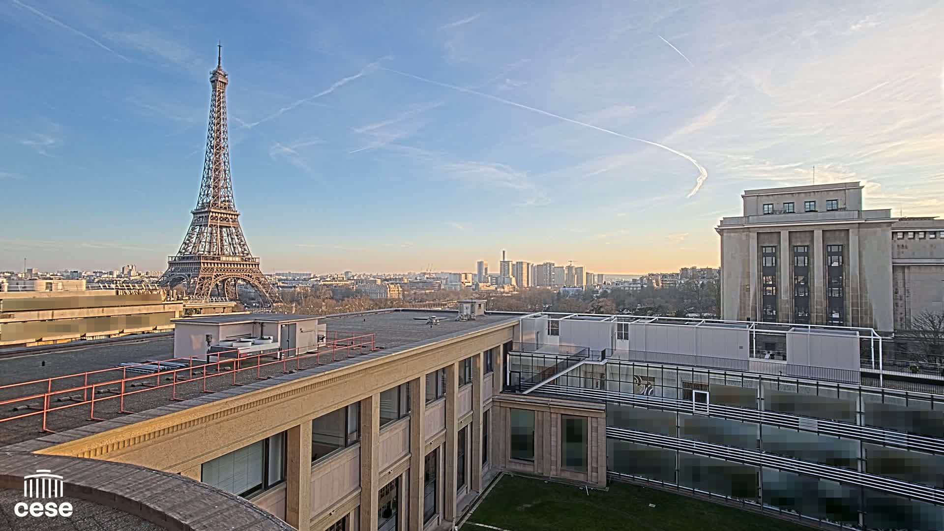 A clear, sunny day reveals the Eiffel Tower in the distance, alongside a city skyline and several buildings, viewed from a rooftop.