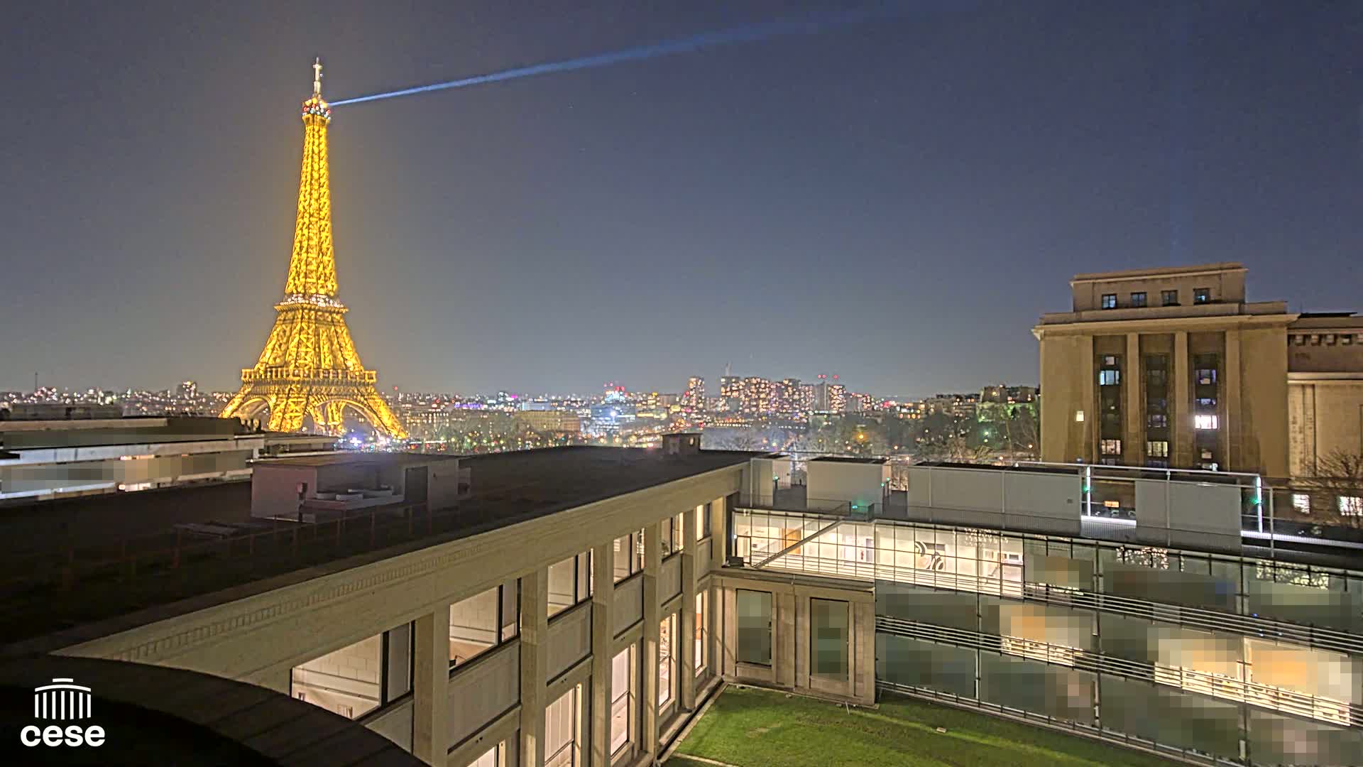 A nighttime view of the Eiffel Tower illuminated, a cityscape, and a modern building with a grassy courtyard.