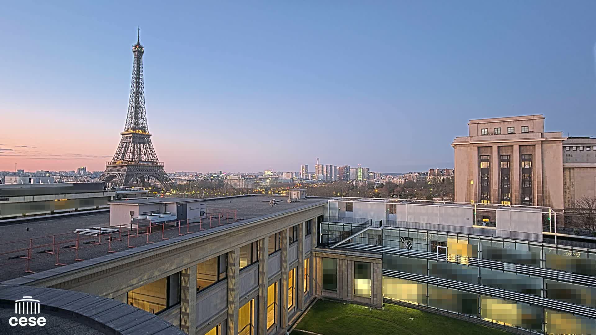 A rooftop view of the Eiffel Tower at dusk, overlooking a city skyline and buildings.