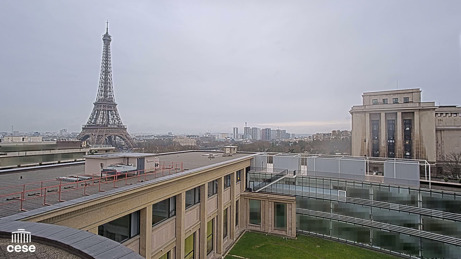 A rooftop view of Parisian buildings on an overcast day, showcasing the Eiffel Tower in the distance.