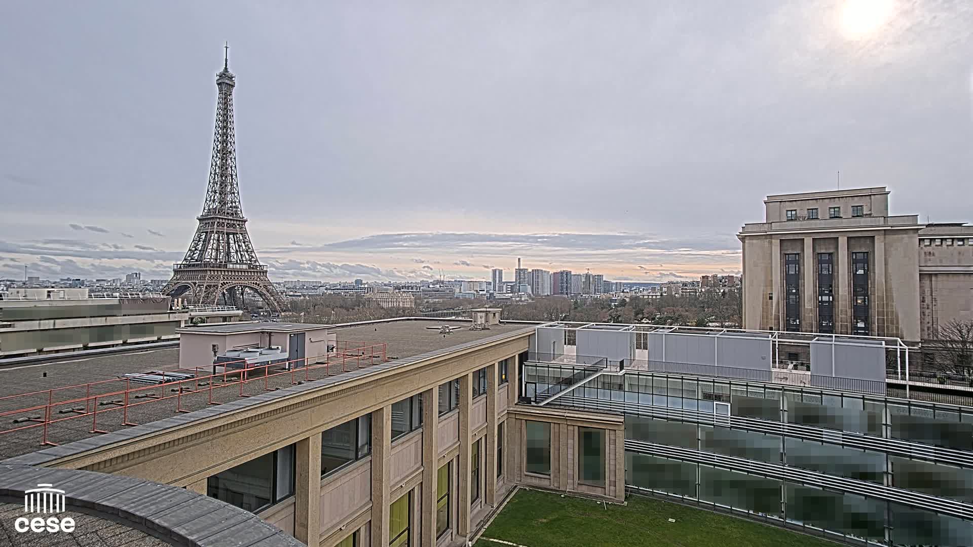 A view of the Eiffel Tower from a rooftop overlooking a city, under an overcast sky.