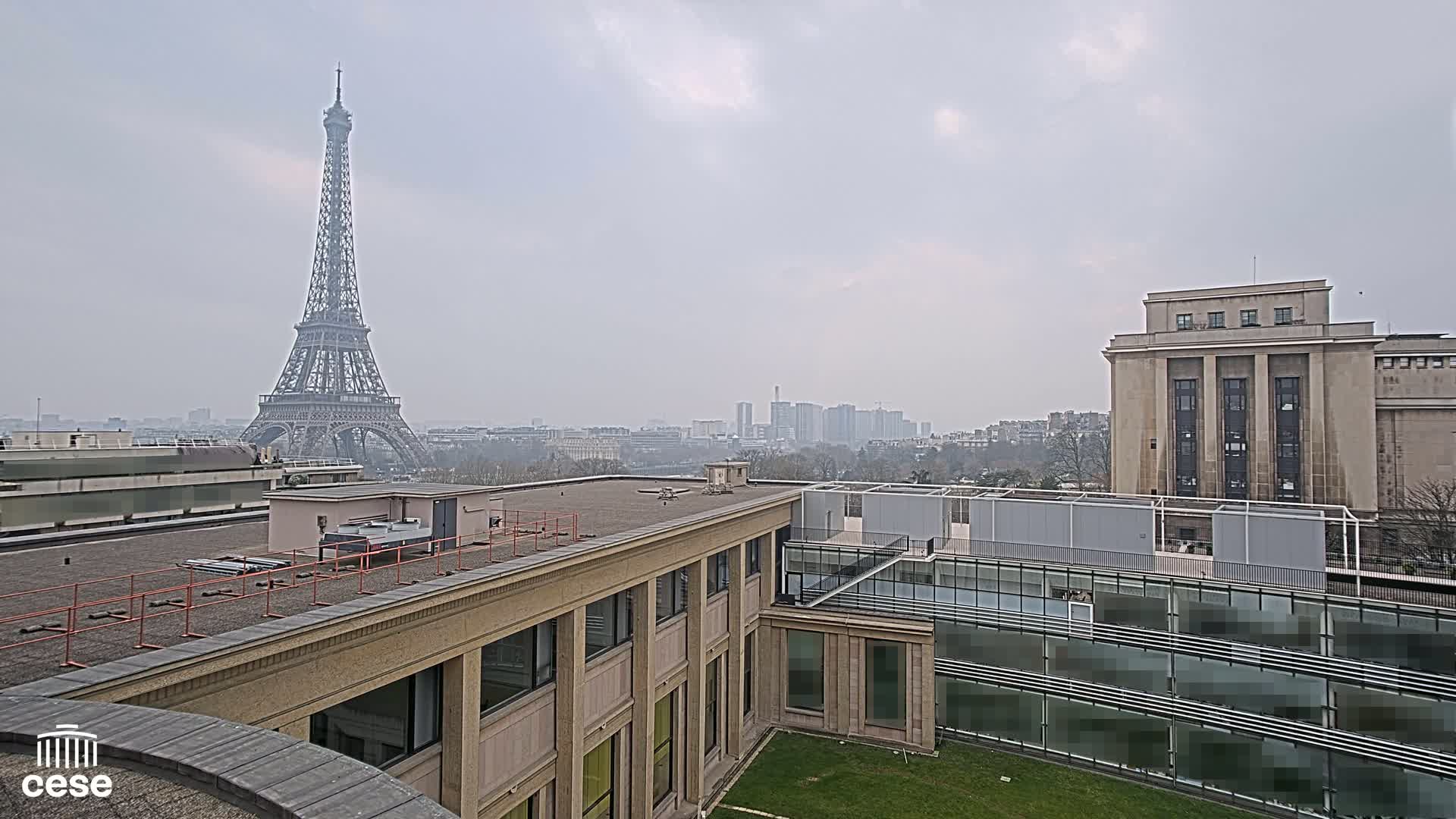 A hazy view of the Eiffel Tower from a rooftop, showing other buildings and a cityscape in the distance.
