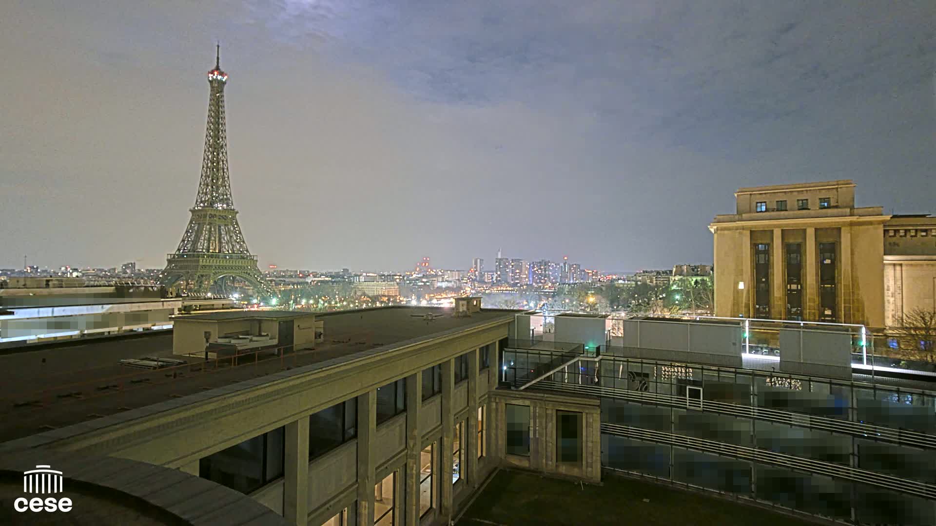 A nighttime view of the Eiffel Tower and Paris city skyline from a rooftop, under a dusky sky.
