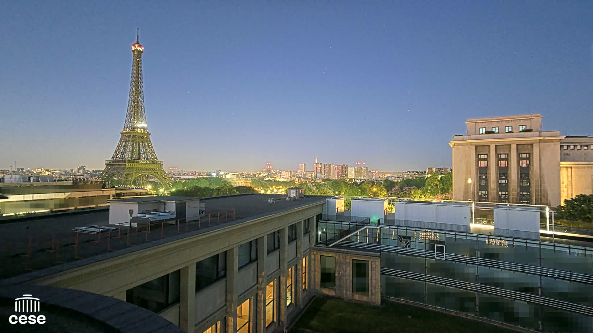 The Eiffel Tower is visible in the distance at twilight, alongside a cityscape and buildings under a clear night sky.