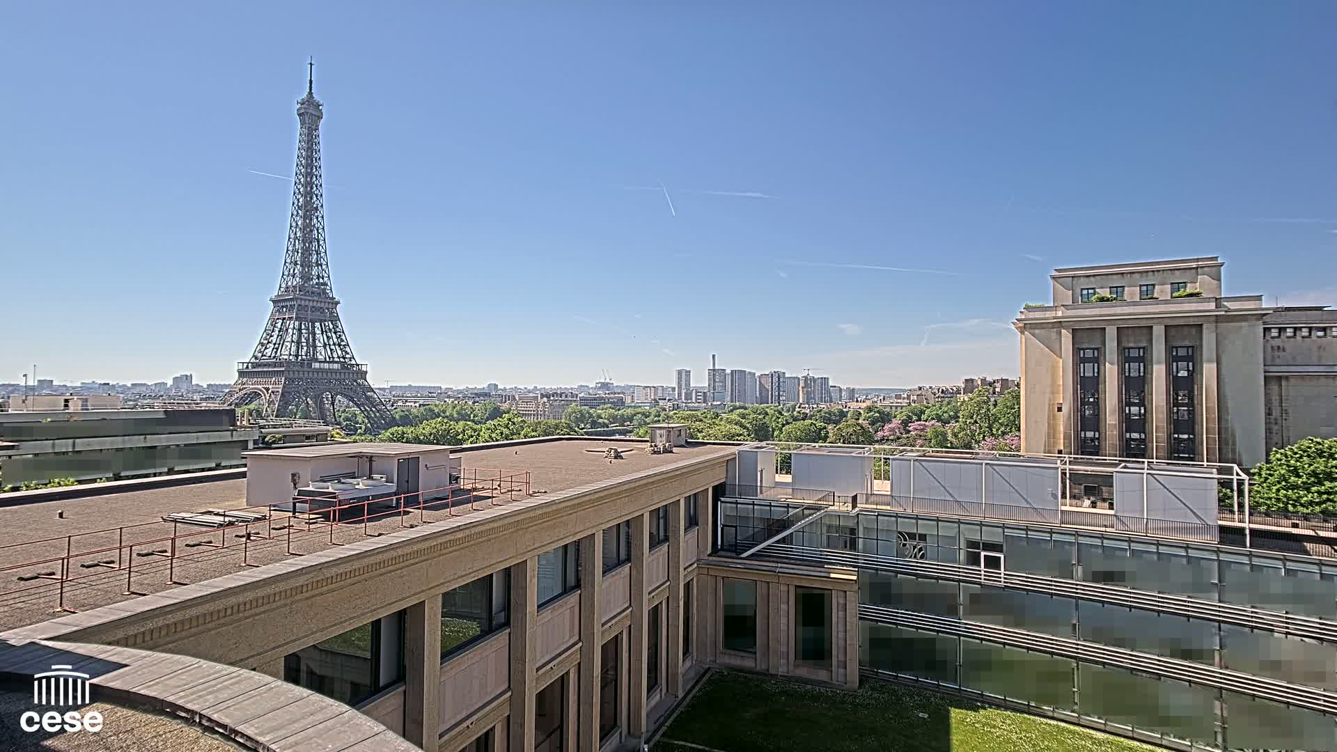 A rooftop view on a clear sunny day shows the Eiffel Tower in the distance, along with a cityscape and other buildings.