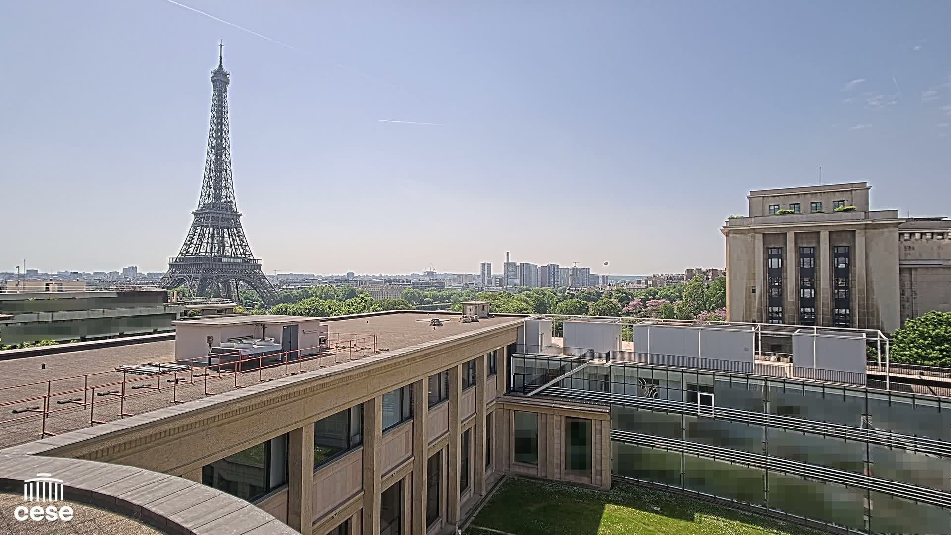 A rooftop view of a Parisian cityscape on a clear, sunny day, showcasing the Eiffel Tower in the distance.