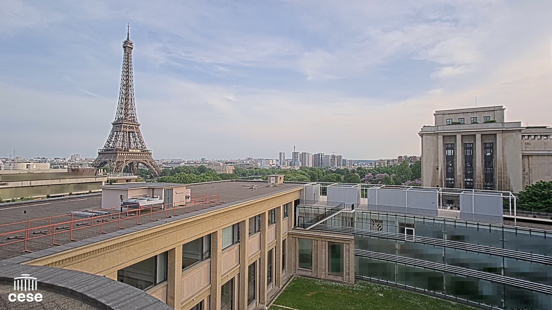 A Parisian cityscape under a partly cloudy sky, featuring the Eiffel Tower in the distance and several modern buildings in the foreground.