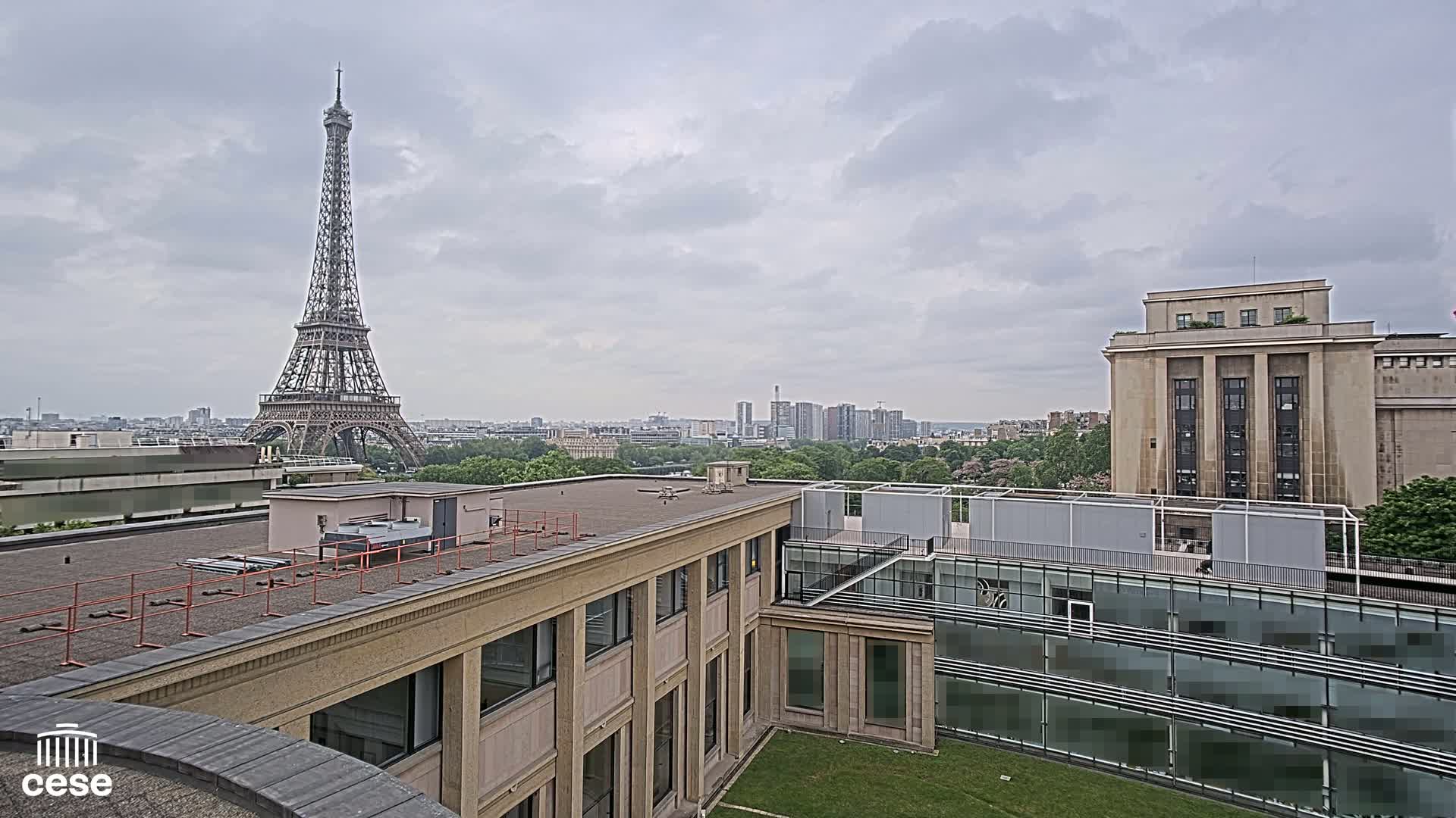 An overcast Parisian cityscape is visible from a rooftop, featuring the Eiffel Tower in the distance and modern and classical buildings in the foreground.