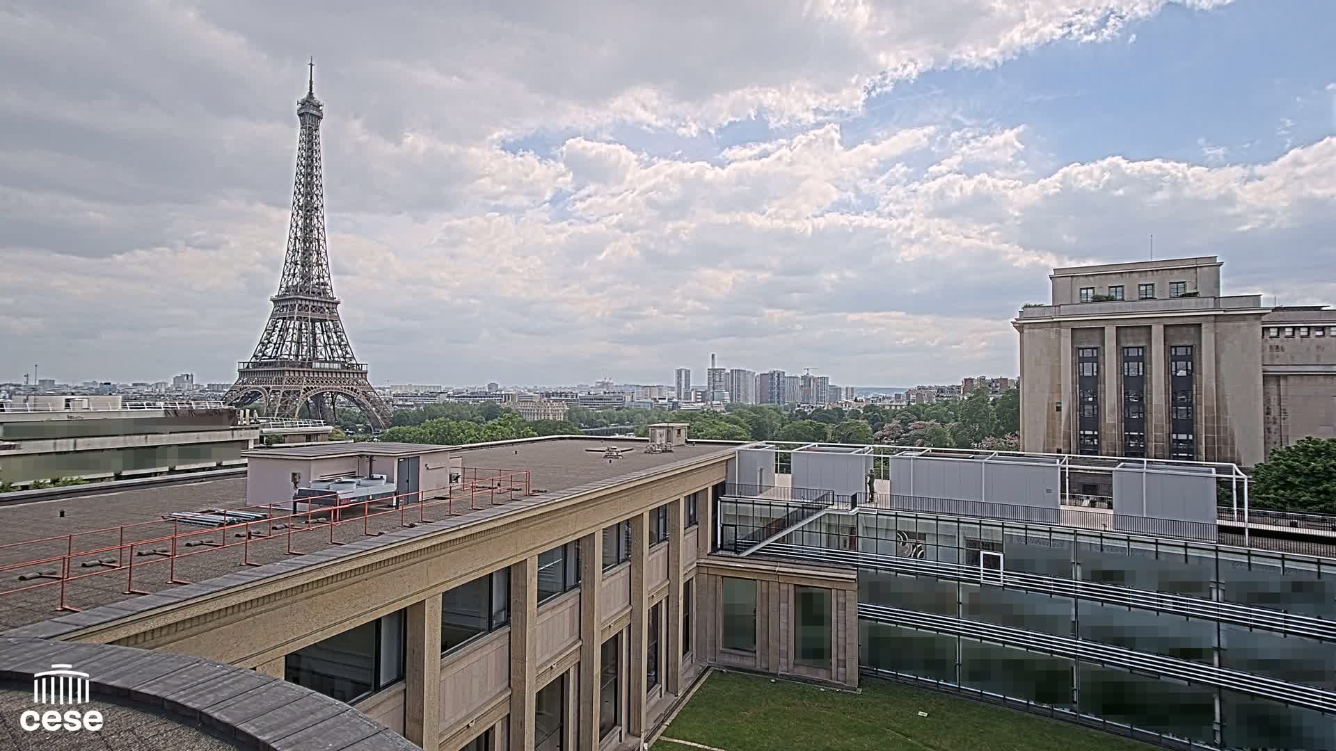 A partly cloudy sky overlooks a city skyline featuring the Eiffel Tower, a large building, and a courtyard with a smaller building.