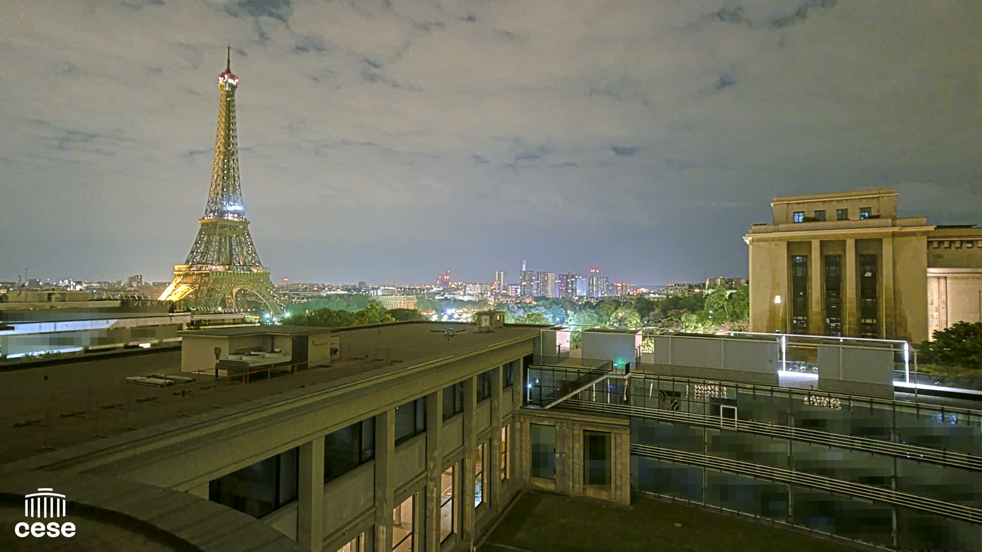A nighttime view of the Eiffel Tower illuminated against a cloudy sky, with city lights and buildings in the foreground.