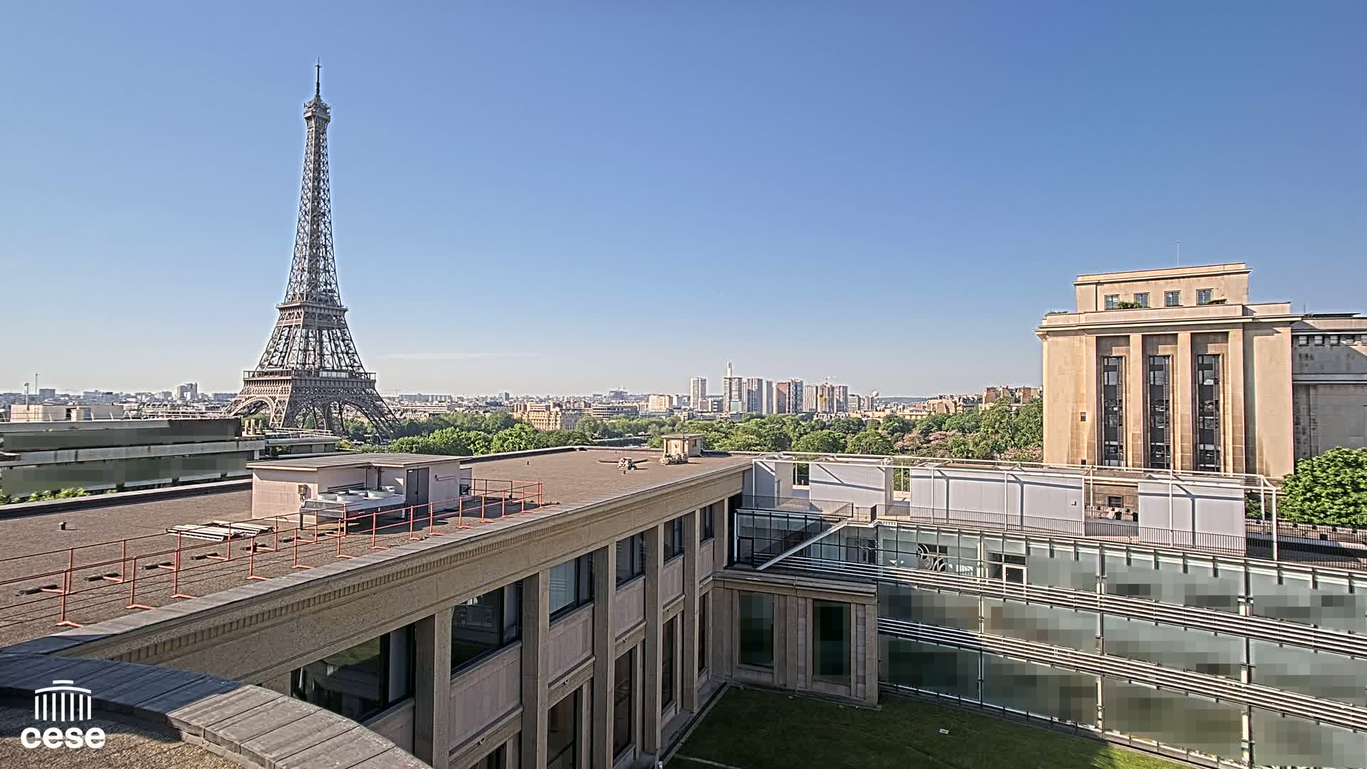A rooftop view of Parisian buildings on a clear, sunny day, showcasing the Eiffel Tower in the distance.