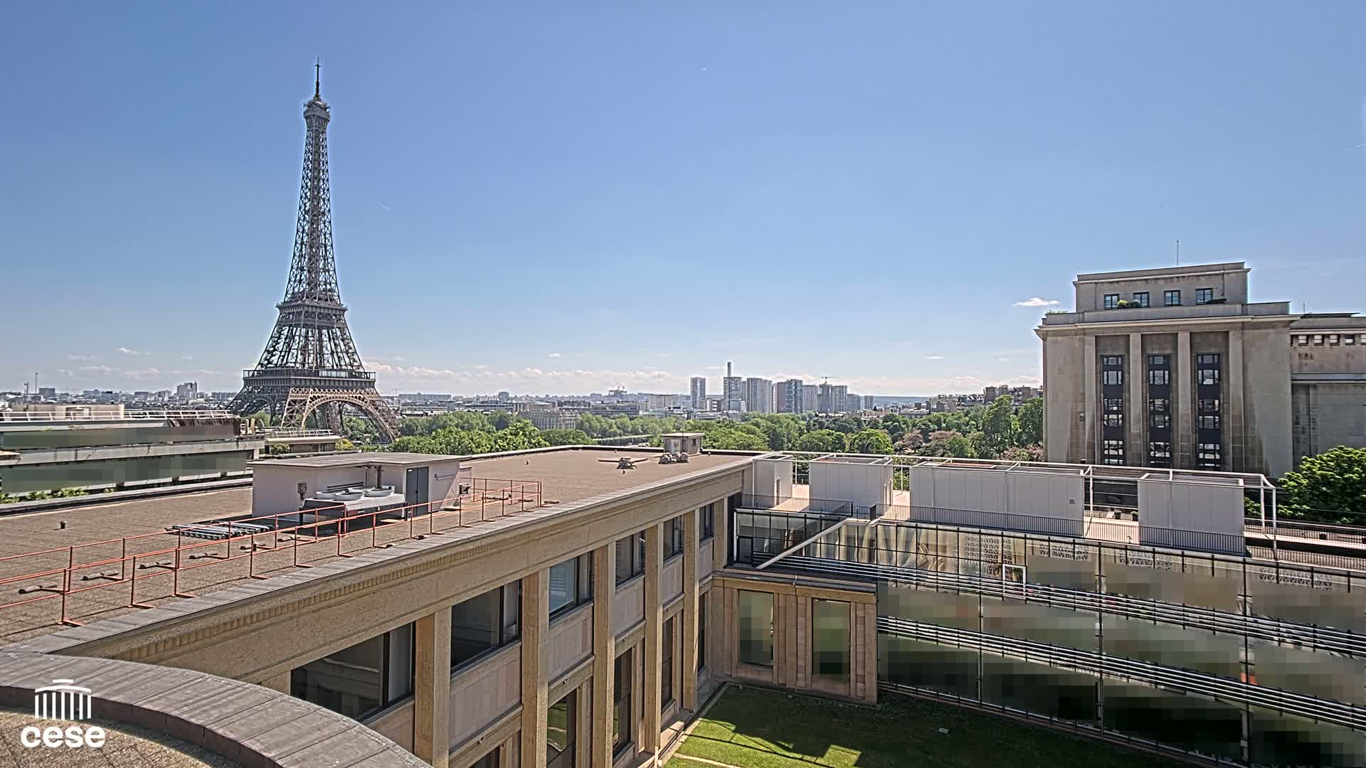 A rooftop view of Paris on a sunny day, showcasing the Eiffel Tower in the distance and other buildings nearby.