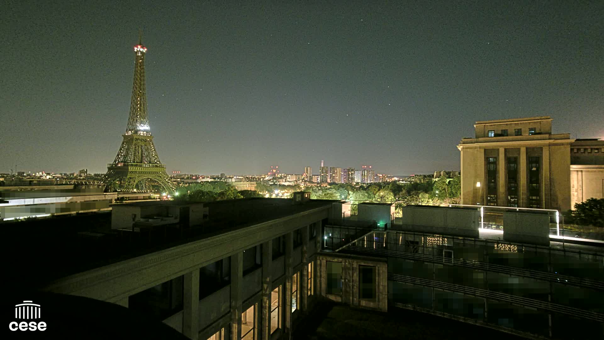 A nighttime view of the Eiffel Tower and a cityscape, with a building in the foreground under a clear, starry sky.