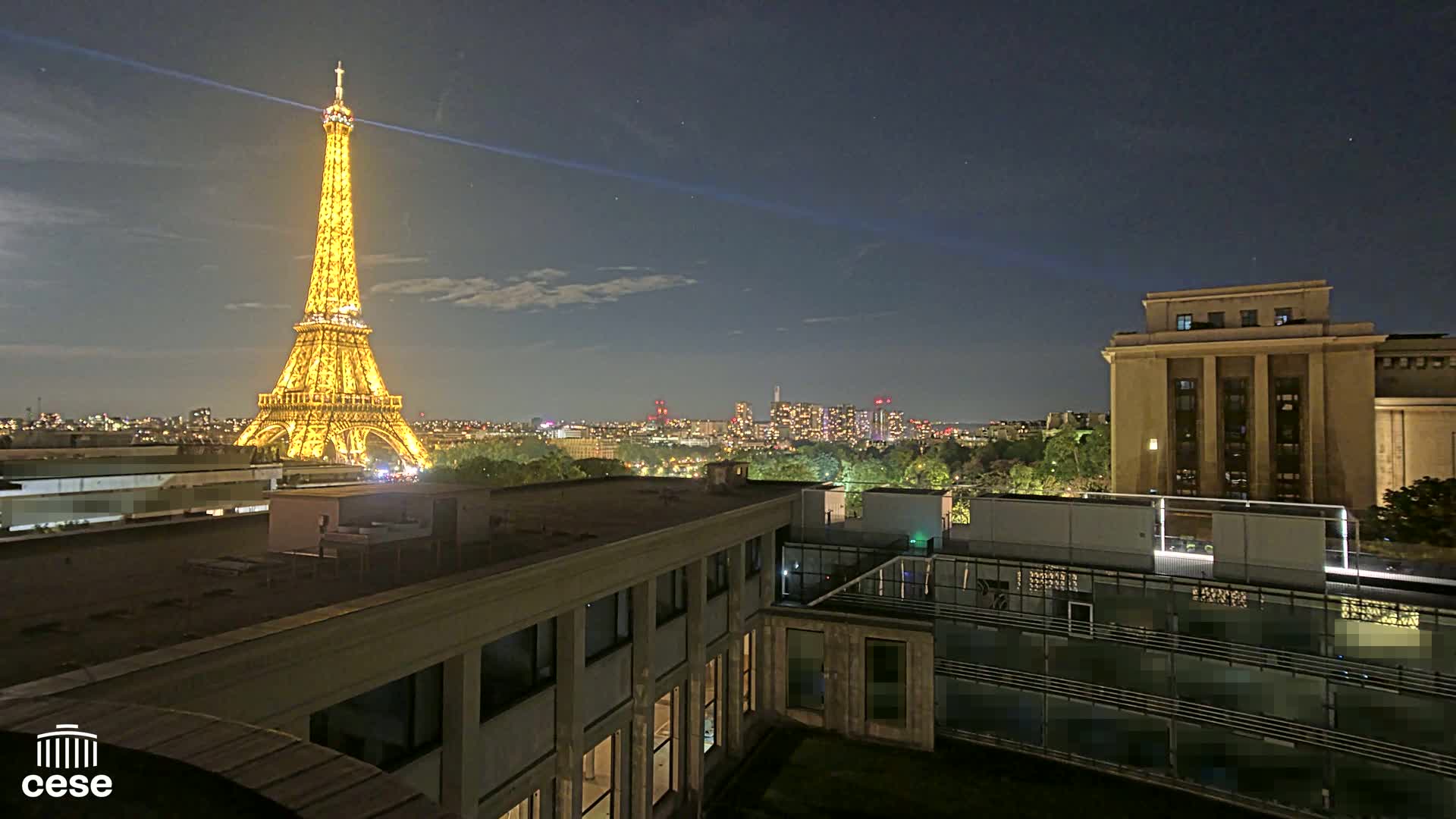 A nighttime view of the Eiffel Tower illuminated, along with a cityscape under a mostly clear sky.