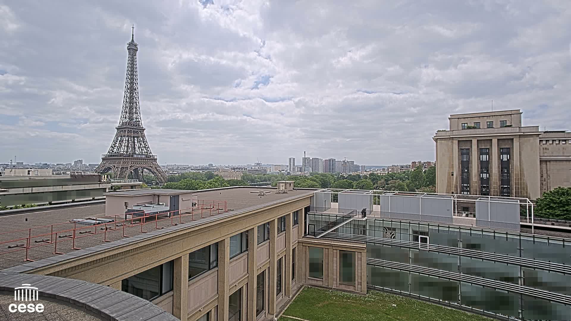 A rooftop view of Parisian buildings on a cloudy day, showing the Eiffel Tower in the distance.