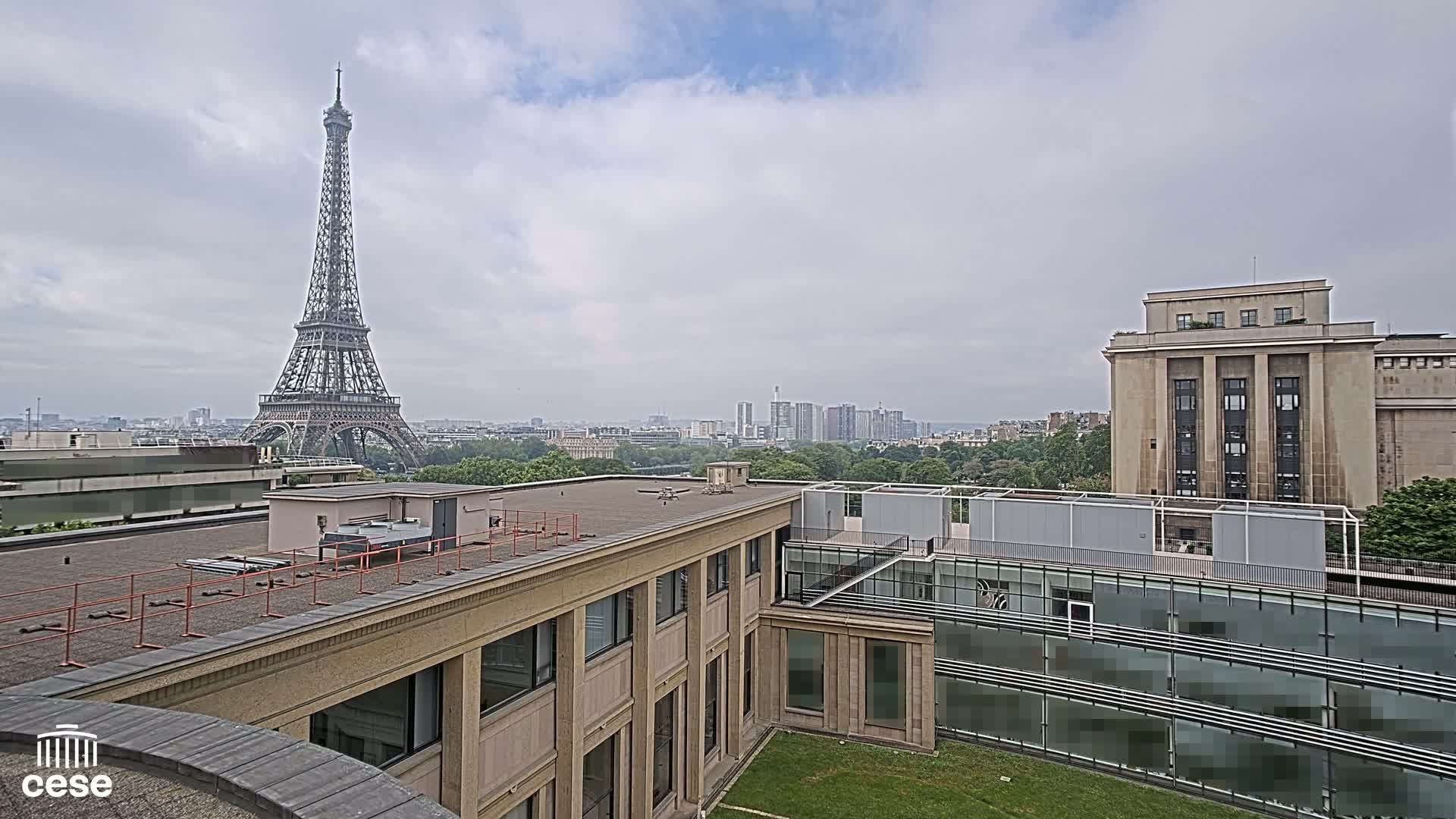 A Parisian cityscape under an overcast sky, featuring the Eiffel Tower in the distance and several modern buildings in the foreground.