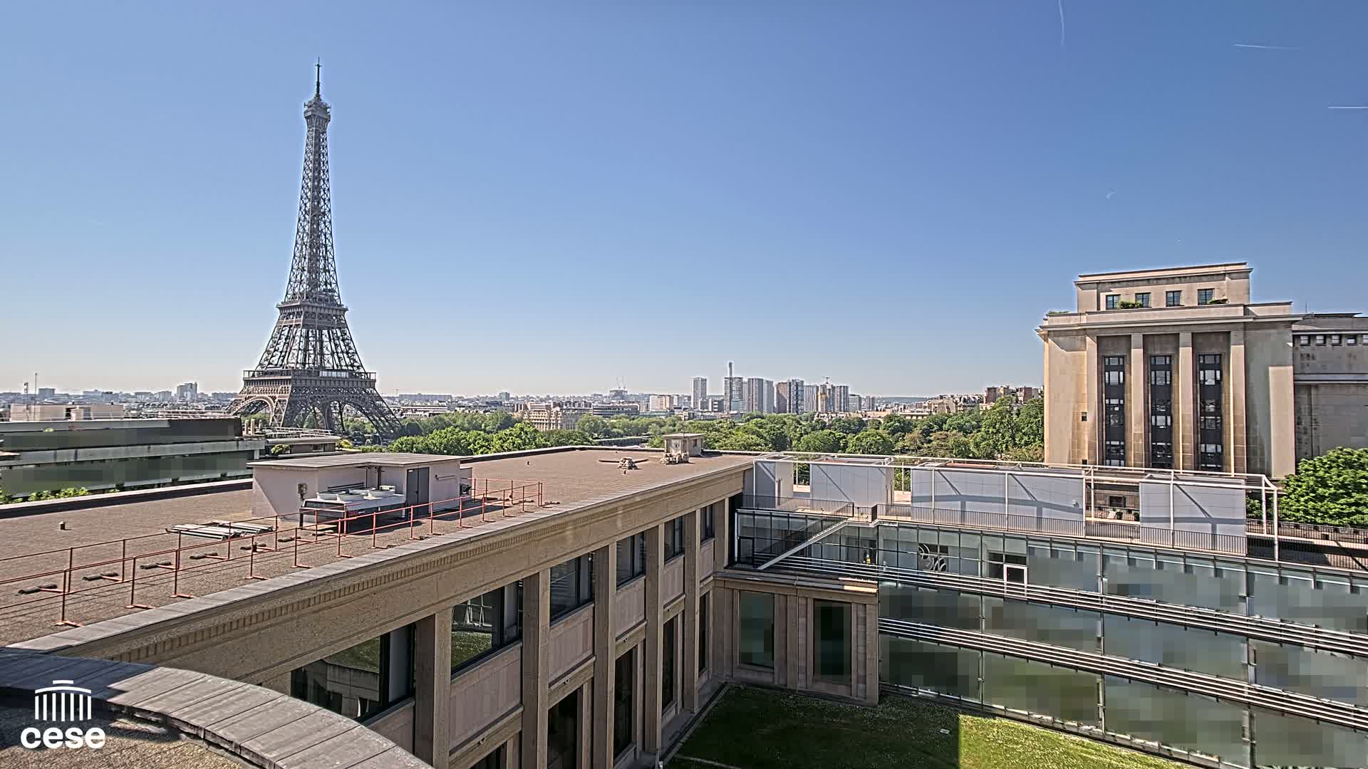 A rooftop view of Parisian buildings, including the Eiffel Tower in the distance, on a clear, sunny day.