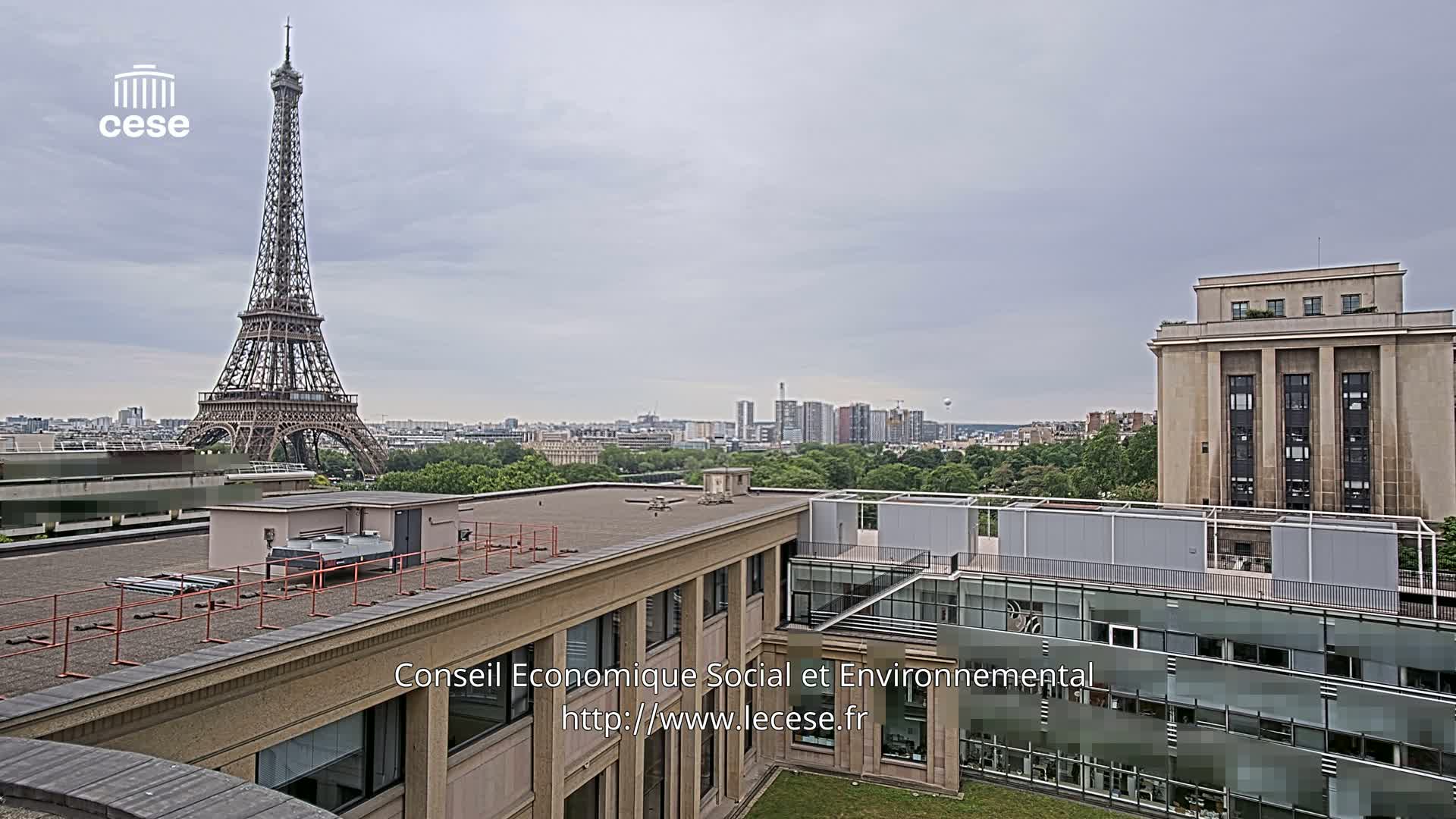 An overcast Parisian cityscape is viewed from a rooftop, showcasing the Eiffel Tower in the distance and modern buildings in the foreground.
